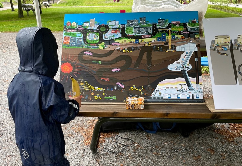 barn i regnkläder tittar på illustraton som visar hur man bygger ut tunnelbanan.