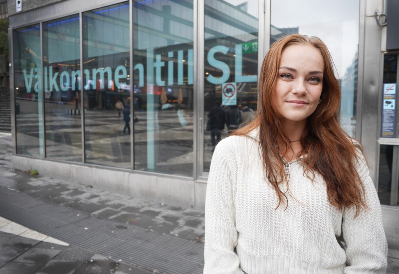 Hanna Lundqvist har långt rödbrunt hår och tittar in i kameran. Hon står utanför SL Kundtjänst på Sergels torg.