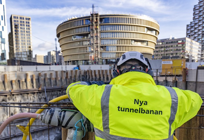 Man i gul  arbetsjacka med texten Nya tunnelbanan på ryggen tittar ut över ett arbetsområde i Hagastaden. 