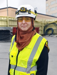 Kvinna med vit bygghjälm, skyddsglasögon och gul varselväst.