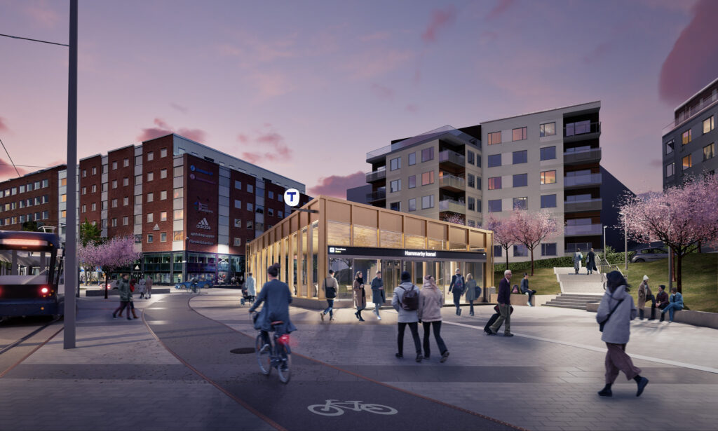 Visionsbild av framtidens tunnelbaneentré vid Hammarby kanal med trästruktur och skyltning, omgiven av människor, körsbärsträd i blom och flerbostadshus i skymningsljus. En spårvagn syns till vänster nära ett rött tegelhus.