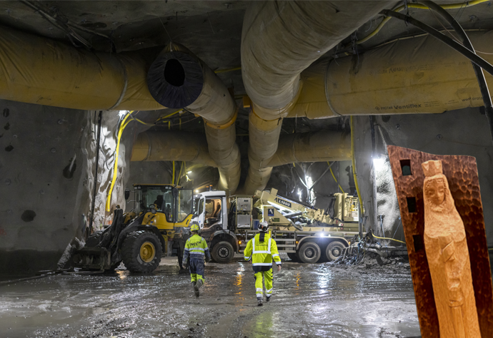 Två arbetare i gul kläder i en tunnel. Montage med en helgonstaty i trä.