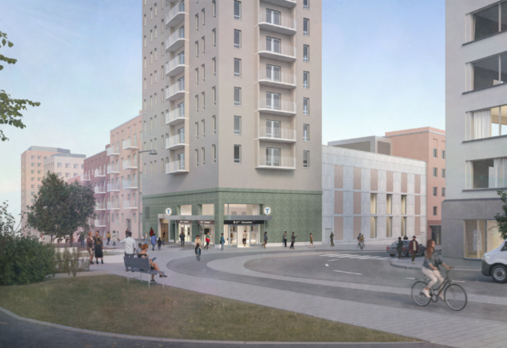 Ett grått och grönt hus med en tunnelbanestation i botten. I förgunden en gång- och cykelbana och en bilväg.