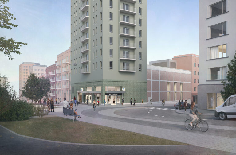 Ett grått och grönt hus med en tunnelbanestation i botten. I förgunden en gång- och cykelbana och en bilväg.