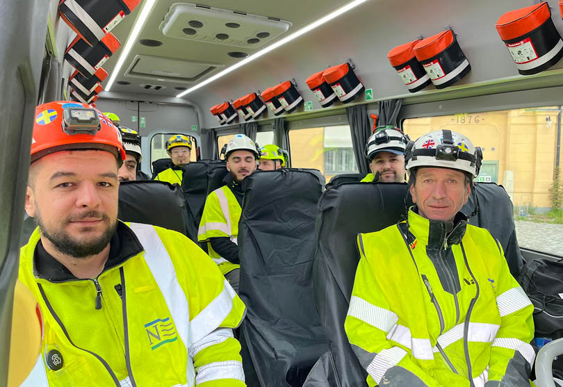 Människor i gula arbetskläder och hjälmar sitter på en buss.