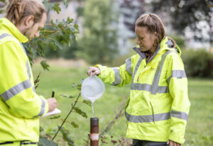 Två personer i varselkläder som fyller på ett grundvattenrör.