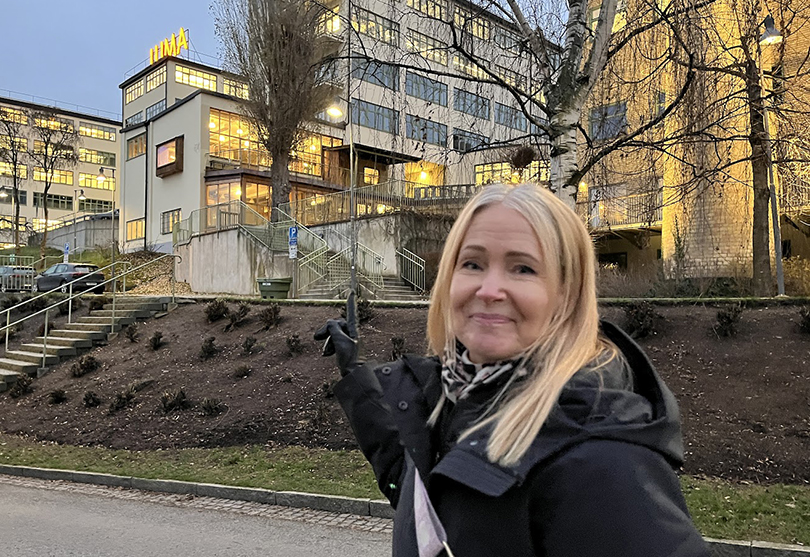 Carina Hed-Pekola i ljust hår och vinterjacka pekar mot upplyst hus med texten Luma.