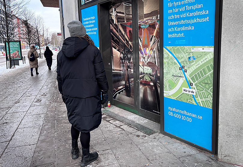 Kvinna med ryggen vänd tittar på skyltning om nya tunnelbanan.