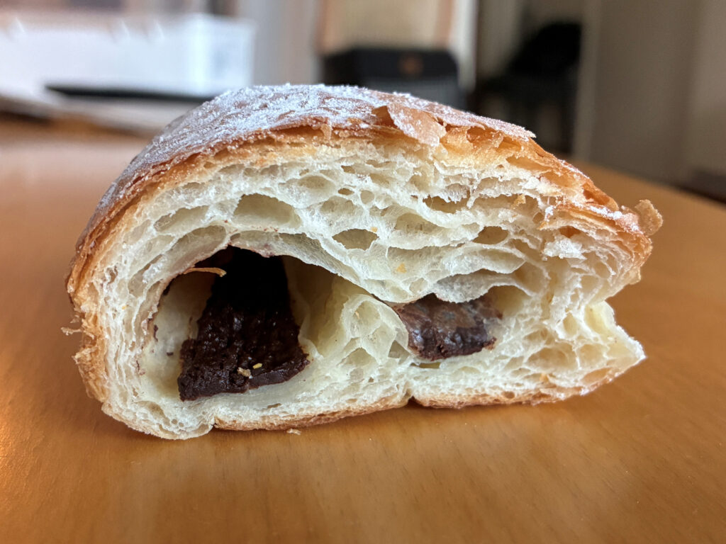 En genomskuren croissant ligger på ett bord och visar en mörk chokladfyllning inuti. Bakgrunden är suddig.