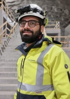 En man iförd skyddsväst och hjälm står framför en trappa.