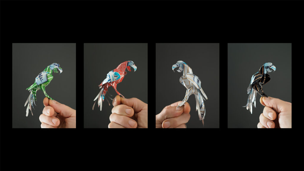 En hand som håller fyra origamifåglar i olika fäger.