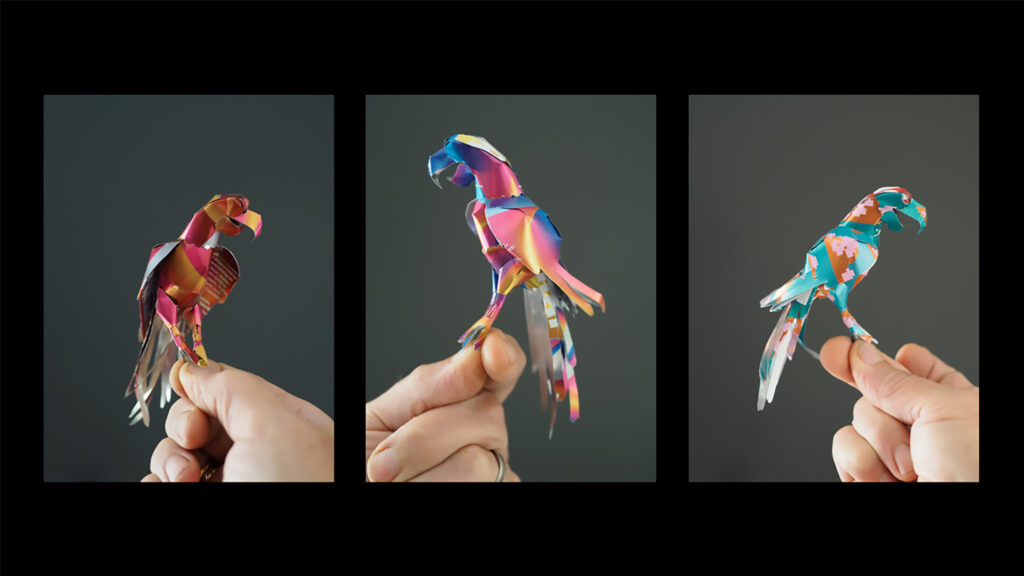 En hand som håller tre origamifåglar i olika fäger.