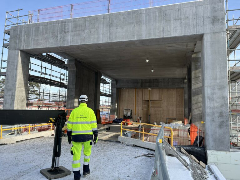 Byggarbetsplats med betongbyggnad och byggnadsarbetare i gula reflexkläder