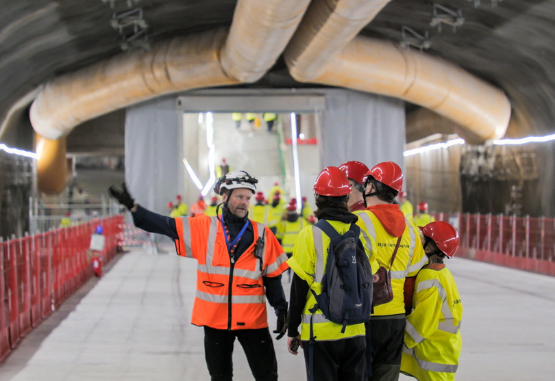 En grupp personer med gula västar står i en tunnel framför en man i orange väst som pekar och förklarar.
