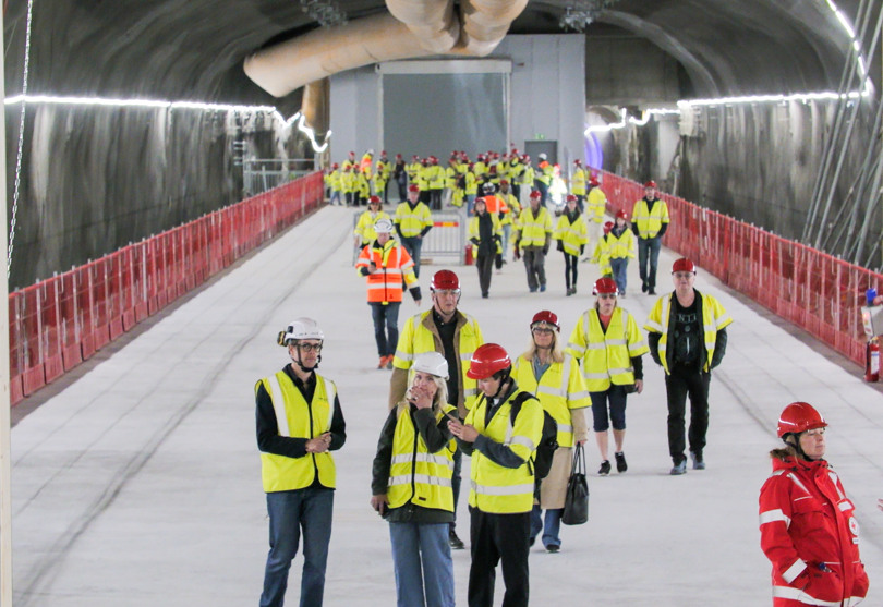 En grupp människor i säkerhetsvästar går på en plattform i en tunnelbanetunnel.