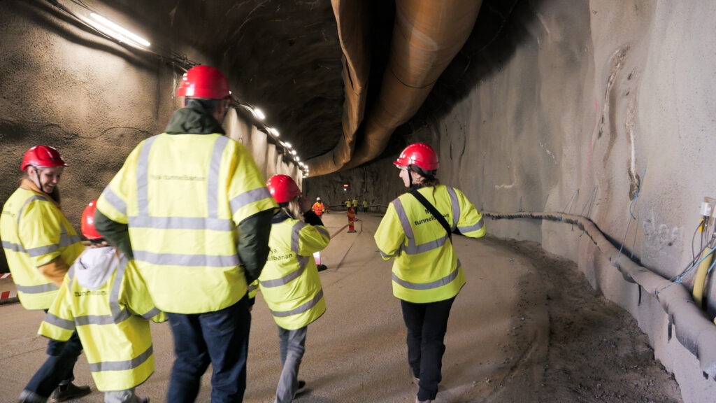 En grupp män i gula jackor och skyddshjälmar går i en tunnel.