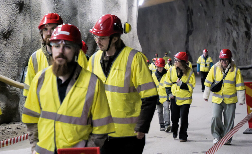 En grupp människor i gula jackor och skyddshjälmar går i en tunnel.