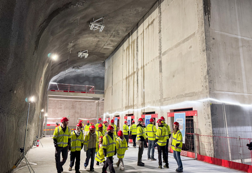En grupp personer i gula jackor står framför en stor betongkonstruktion i en tunnel.