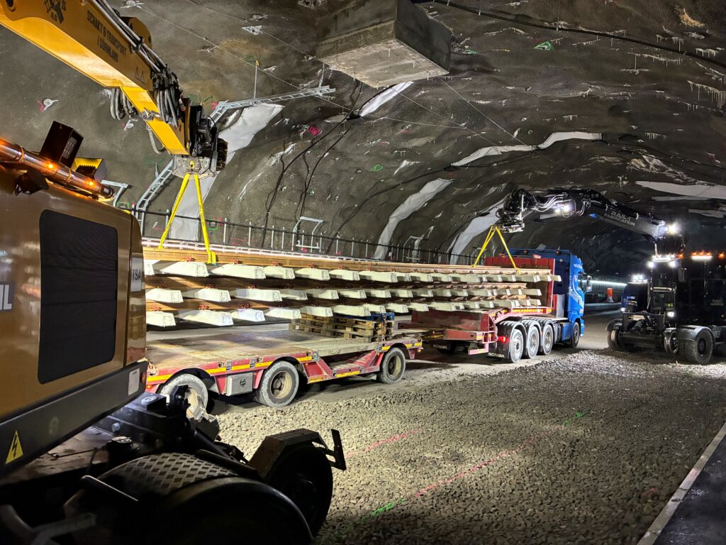 I en tunnel står en lastbil med släp lastad med långa delar av räls och slipers.